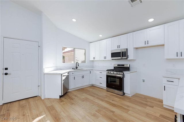 kitchen with stainless steel appliances, sink, white cabinets, and light hardwood / wood-style floors