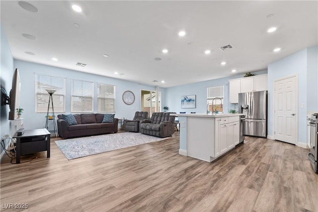 kitchen with appliances with stainless steel finishes, light hardwood / wood-style flooring, an island with sink, and white cabinets