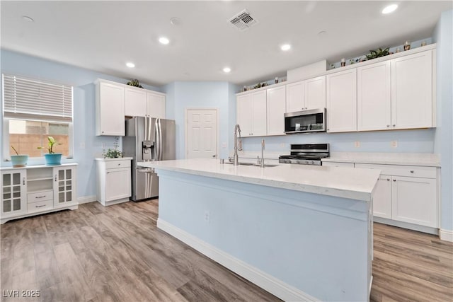 kitchen featuring light wood-type flooring, a center island with sink, sink, appliances with stainless steel finishes, and white cabinets