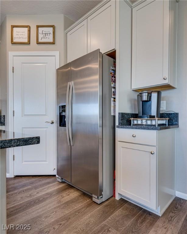 kitchen with hardwood / wood-style floors, white cabinetry, dark stone counters, and stainless steel refrigerator with ice dispenser