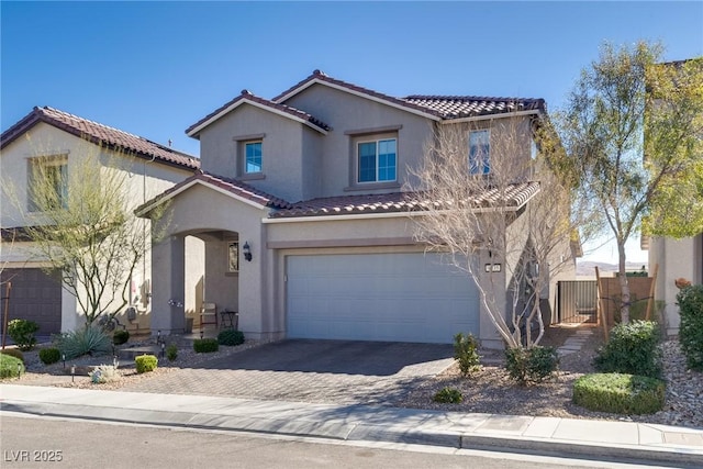 mediterranean / spanish home with a tiled roof, an attached garage, fence, decorative driveway, and stucco siding