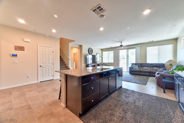 kitchen featuring a kitchen island with sink, light stone countertops, sink, light tile patterned floors, and a kitchen breakfast bar