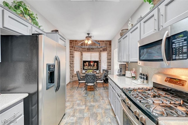 kitchen featuring ceiling fan, brick wall, stone finish floor, appliances with stainless steel finishes, and light countertops