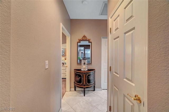 hallway with visible vents, a textured wall, and light tile patterned flooring