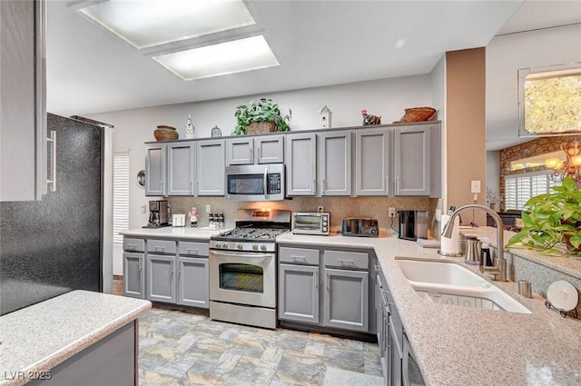 kitchen featuring a toaster, gray cabinets, stainless steel appliances, and a sink