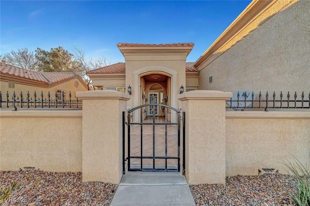 entrance to property featuring a gate, a tile roof, fence, and stucco siding