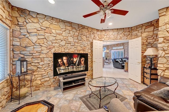 living room with stone finish flooring, a fireplace, and a ceiling fan