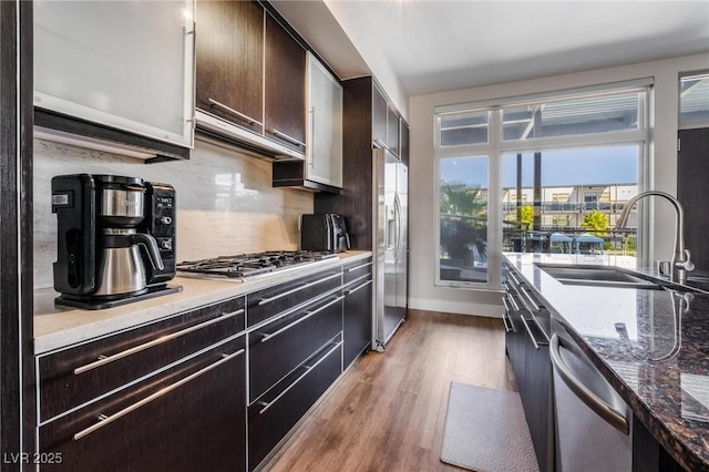 kitchen featuring stainless steel appliances, dark brown cabinetry, light hardwood / wood-style floors, backsplash, and sink