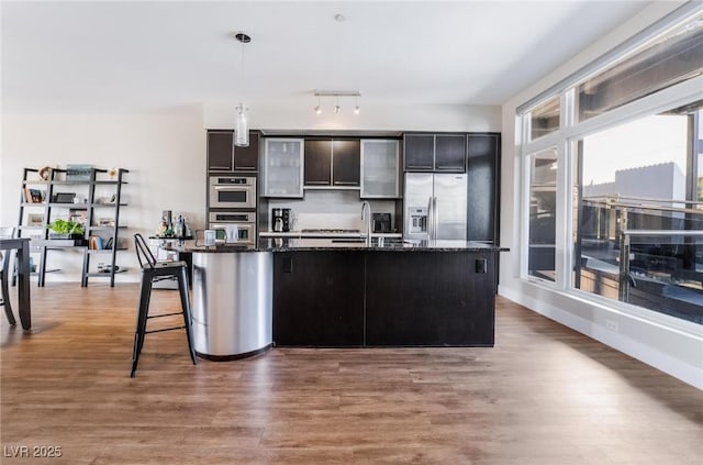 kitchen featuring appliances with stainless steel finishes, decorative light fixtures, a kitchen island with sink, and dark stone countertops