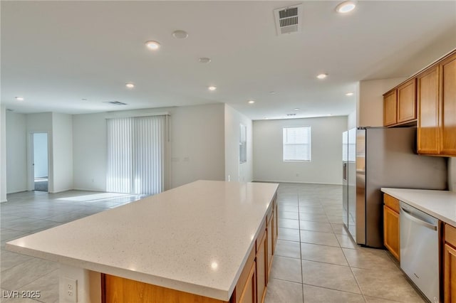 kitchen featuring light tile patterned floors, stainless steel appliances, a kitchen island, and light stone counters