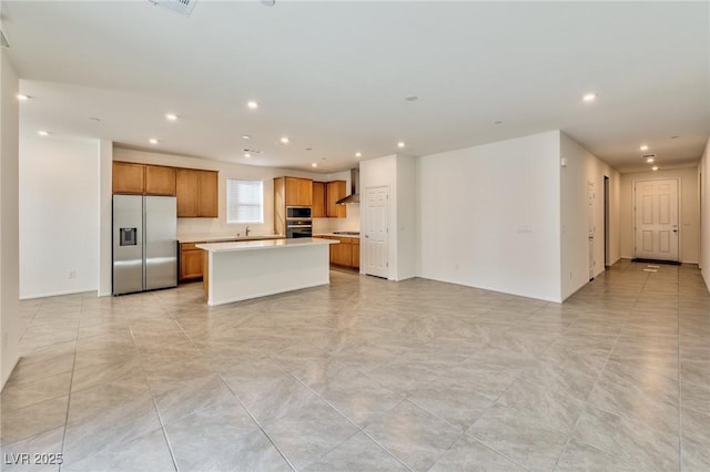 kitchen with wall chimney range hood, stainless steel refrigerator with ice dispenser, a center island, sink, and oven