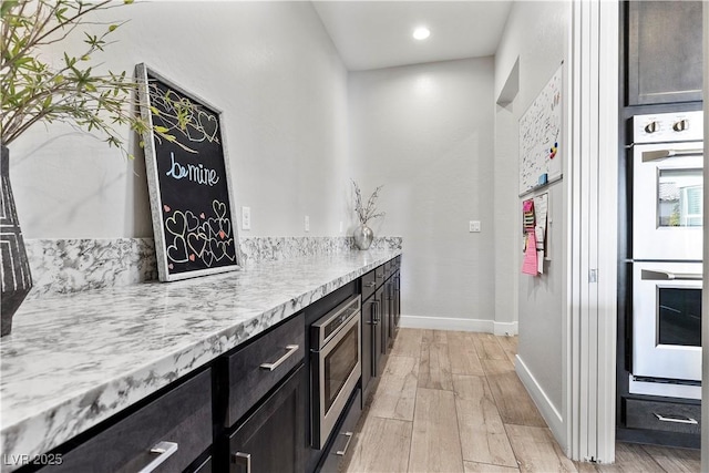 kitchen with light hardwood / wood-style flooring, double wall oven, dark brown cabinets, light stone counters, and stainless steel microwave