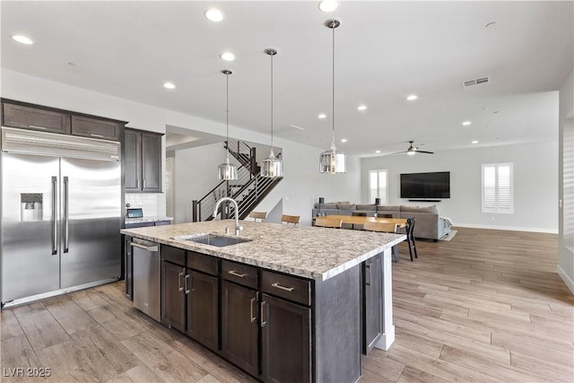 kitchen featuring a center island with sink, sink, decorative light fixtures, stainless steel appliances, and dark brown cabinets