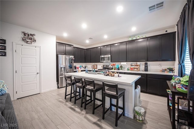 kitchen with light hardwood / wood-style floors, a kitchen bar, stainless steel appliances, and a kitchen island