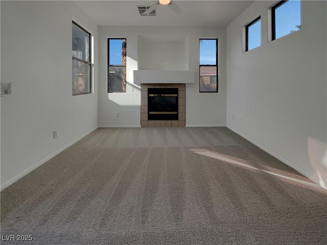 unfurnished living room with a tiled fireplace, light colored carpet, and ceiling fan