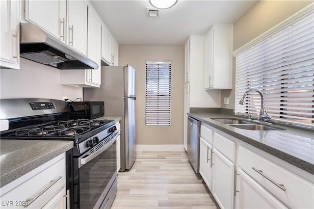 kitchen featuring dark stone countertops, light hardwood / wood-style flooring, sink, appliances with stainless steel finishes, and white cabinets