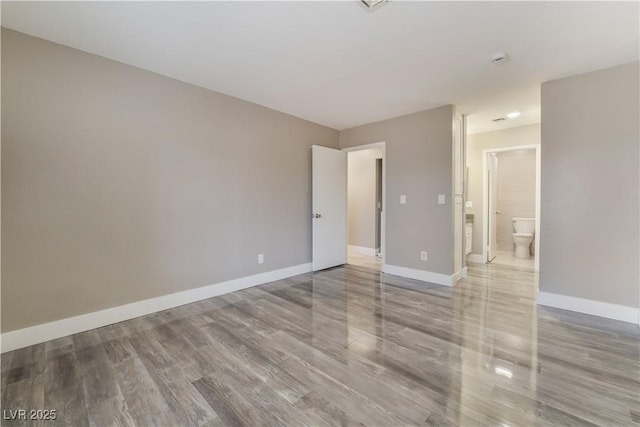 unfurnished bedroom with ensuite bath and wood-type flooring