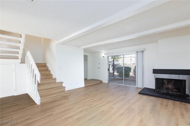 unfurnished living room with light hardwood / wood-style floors, a textured ceiling, and beam ceiling