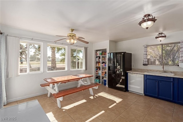 kitchen with light tile patterned floors, sink, blue cabinets, black fridge, and white dishwasher