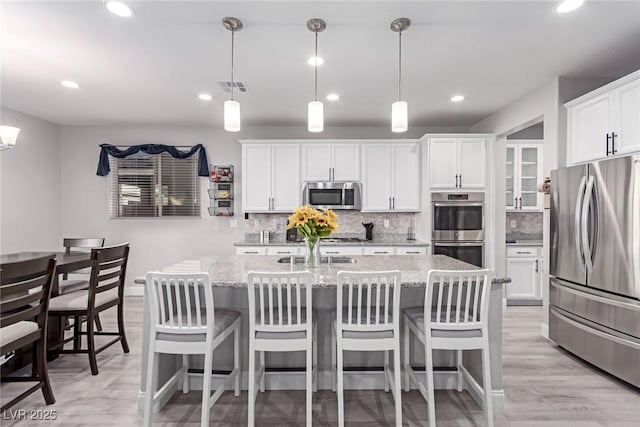 kitchen featuring white cabinetry, appliances with stainless steel finishes, hanging light fixtures, and light stone counters