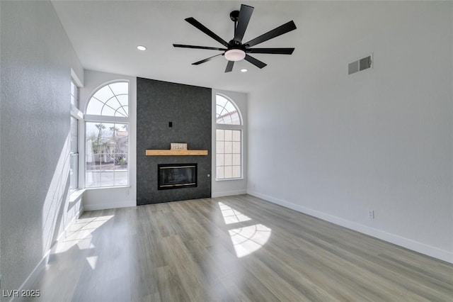 unfurnished living room with plenty of natural light, ceiling fan, a large fireplace, and light hardwood / wood-style flooring