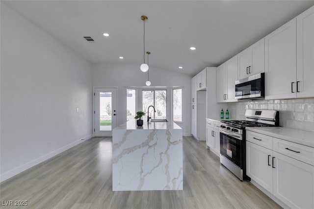 kitchen with white cabinets, appliances with stainless steel finishes, light stone countertops, and decorative light fixtures