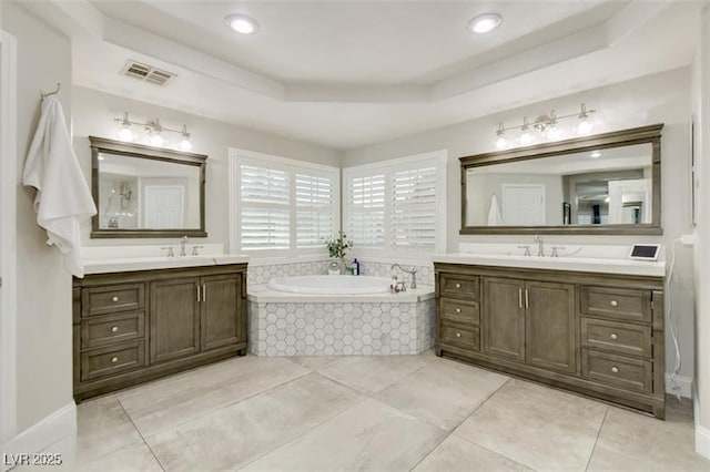 bathroom with tiled bath, tile patterned floors, a tray ceiling, and vanity