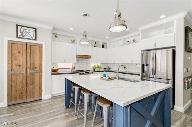 kitchen featuring sink, a kitchen island with sink, white cabinets, and stainless steel fridge