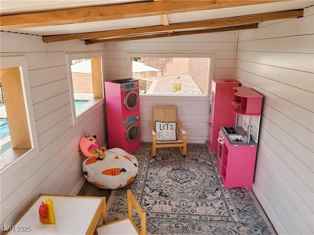 game room with wooden walls and stacked washer and clothes dryer