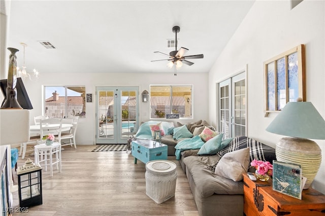 living room featuring ceiling fan with notable chandelier, french doors, light hardwood / wood-style flooring, and lofted ceiling