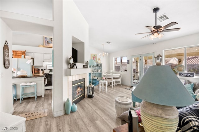 living room featuring ceiling fan with notable chandelier, plenty of natural light, light wood-type flooring, and vaulted ceiling