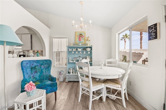 dining space with hardwood / wood-style floors, vaulted ceiling, and a notable chandelier