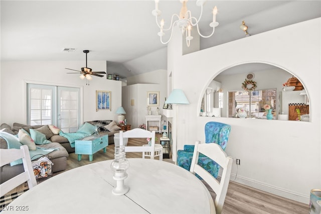 dining area featuring ceiling fan with notable chandelier, light hardwood / wood-style flooring, vaulted ceiling, and french doors