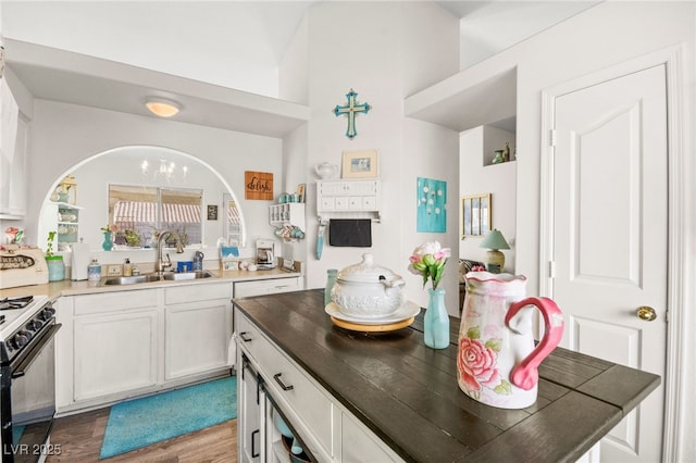 kitchen with a chandelier, wood-type flooring, sink, black gas range, and white cabinets