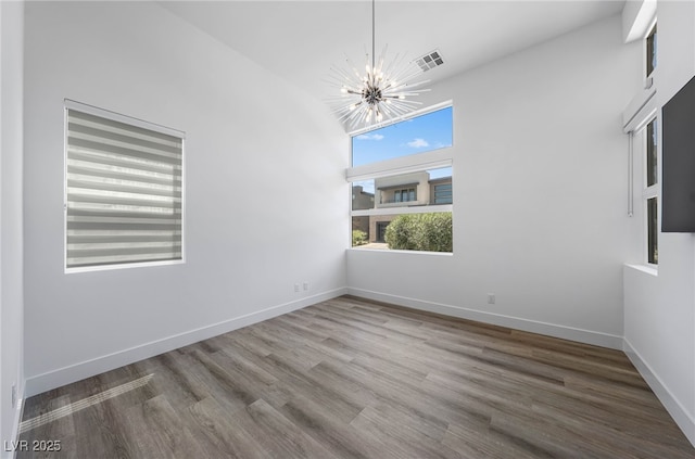 spare room with hardwood / wood-style flooring, a towering ceiling, and a notable chandelier