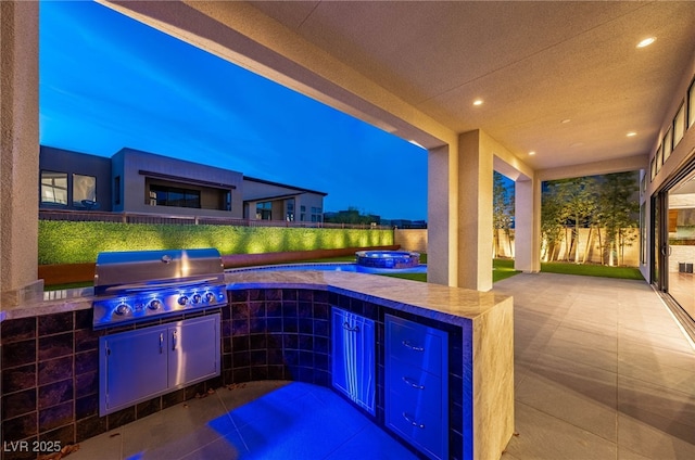 patio terrace at dusk with an outdoor kitchen, area for grilling, and an in ground hot tub