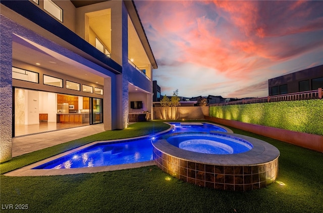 pool at dusk with a lawn, a patio, and an in ground hot tub