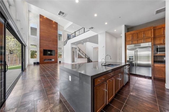 kitchen with a kitchen island with sink, a towering ceiling, built in appliances, sink, and dark tile patterned flooring