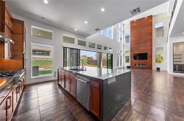 kitchen featuring dishwasher, an island with sink, a towering ceiling, cooktop, and sink