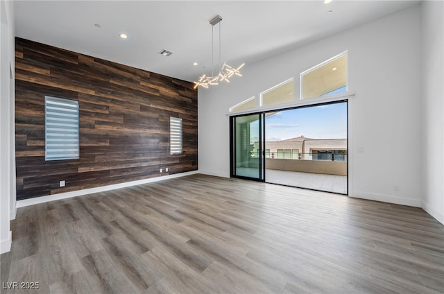 spare room featuring hardwood / wood-style floors, a notable chandelier, wood walls, and a high ceiling