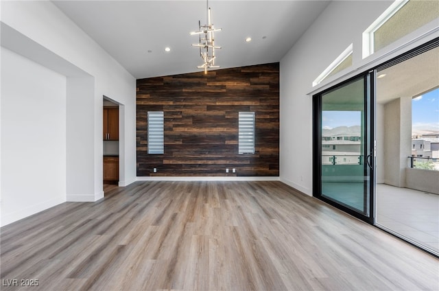 spare room featuring light wood-type flooring, a chandelier, wood walls, and a towering ceiling