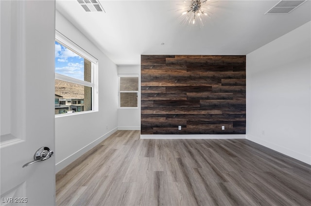 spare room with wood walls, a notable chandelier, and light hardwood / wood-style flooring