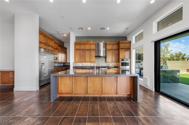 kitchen with a center island with sink, built in appliances, sink, wall chimney range hood, and decorative backsplash