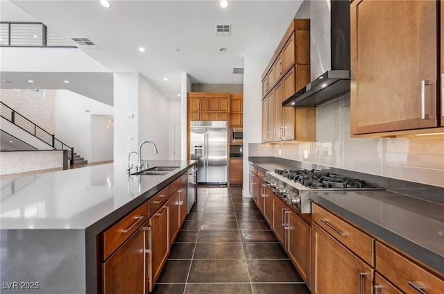 kitchen featuring a center island with sink, built in appliances, sink, wall chimney exhaust hood, and tasteful backsplash