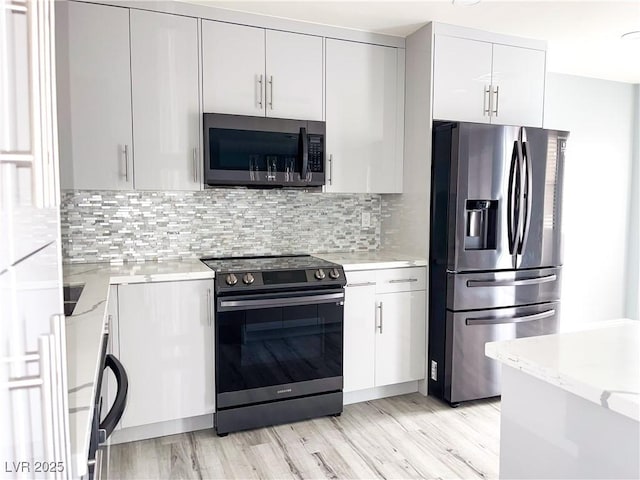 kitchen with stainless steel appliances, light hardwood / wood-style floors, backsplash, light stone counters, and white cabinets