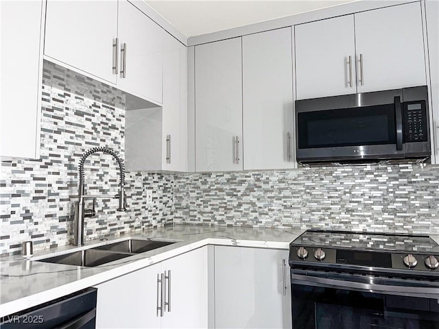 kitchen with stainless steel appliances, light stone countertops, sink, tasteful backsplash, and white cabinets