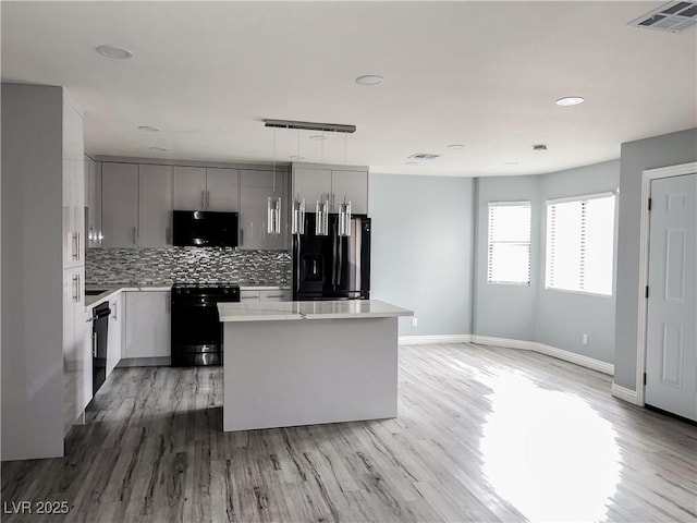 kitchen featuring tasteful backsplash, gray cabinetry, black appliances, a center island, and light wood-type flooring