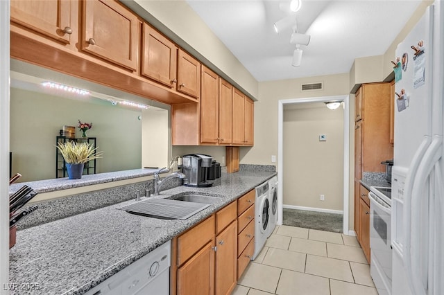 kitchen featuring white appliances, light stone countertops, washer / dryer, light tile patterned floors, and sink