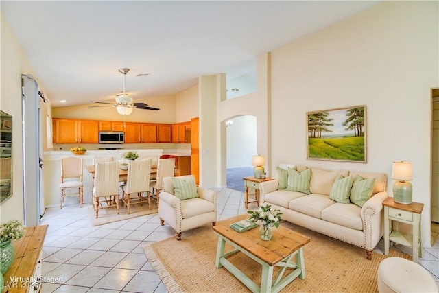 living area with light tile patterned floors, arched walkways, ceiling fan, and vaulted ceiling