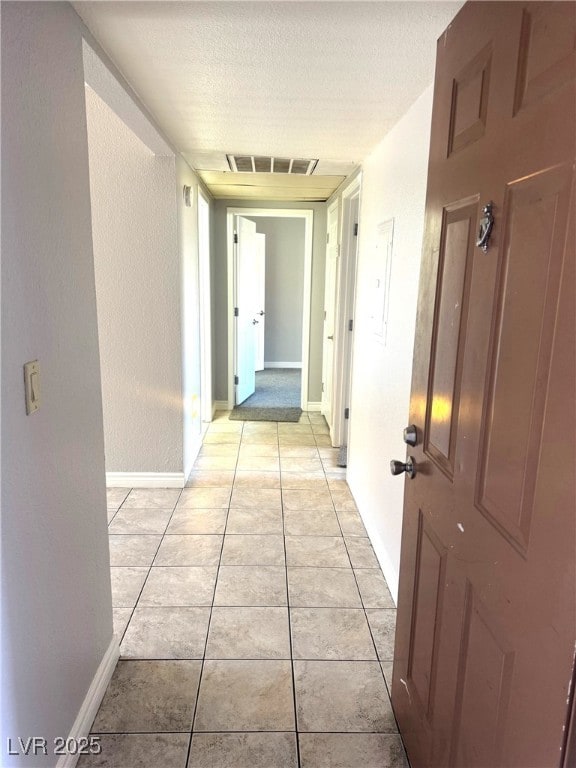 hall with a textured ceiling and light tile patterned floors